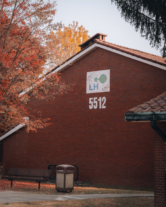 services-img Red brick building in fall, with trees and a bench, featuring signage.